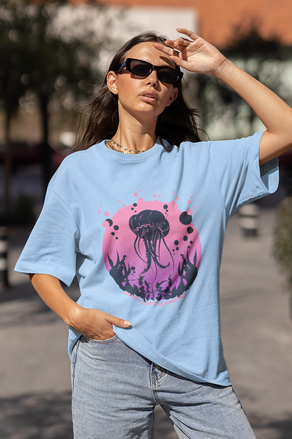 Woman wearing Baby blue oversized 240 GSM t-shirt with pink and purple jellyfish ocean design and “Beauty Can’t Be Touched” text.