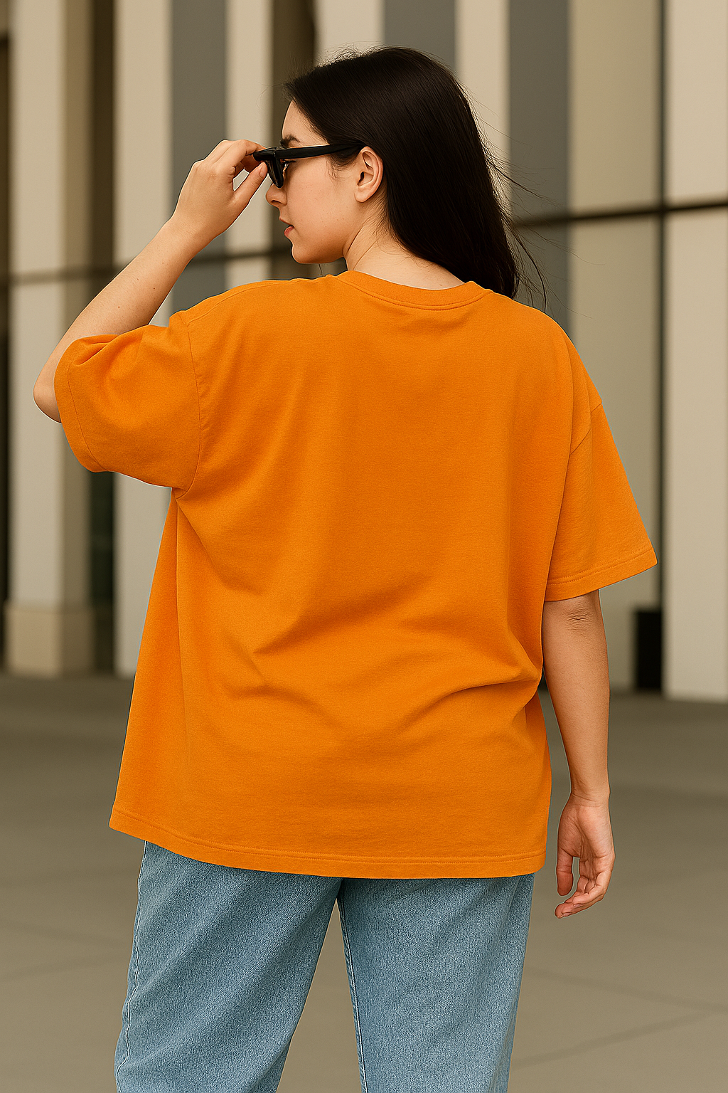Woman wearing an oversized orange graphic t-shirt featuring an anime-style girl with sunglasses and the text "Consciously Chronic Cute", posing confidently with jeans and dark sunglasses.