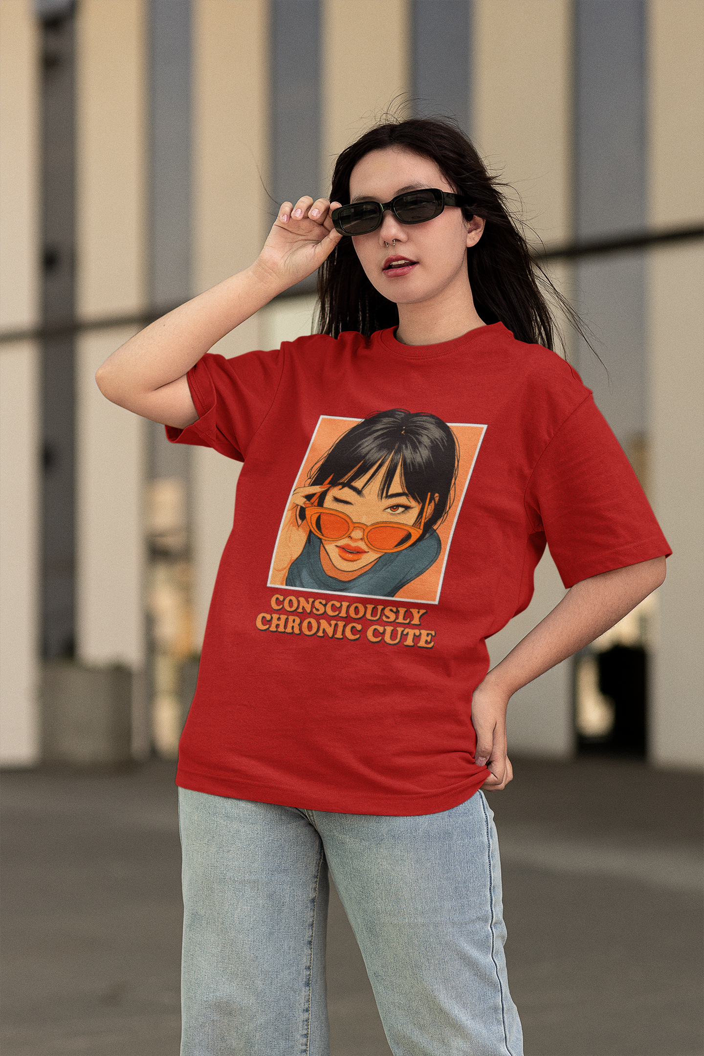 Woman wearing an oversized red graphic t-shirt featuring an anime-style girl with sunglasses and the text "Consciously Chronic Cute", posing confidently with jeans and dark sunglasses.