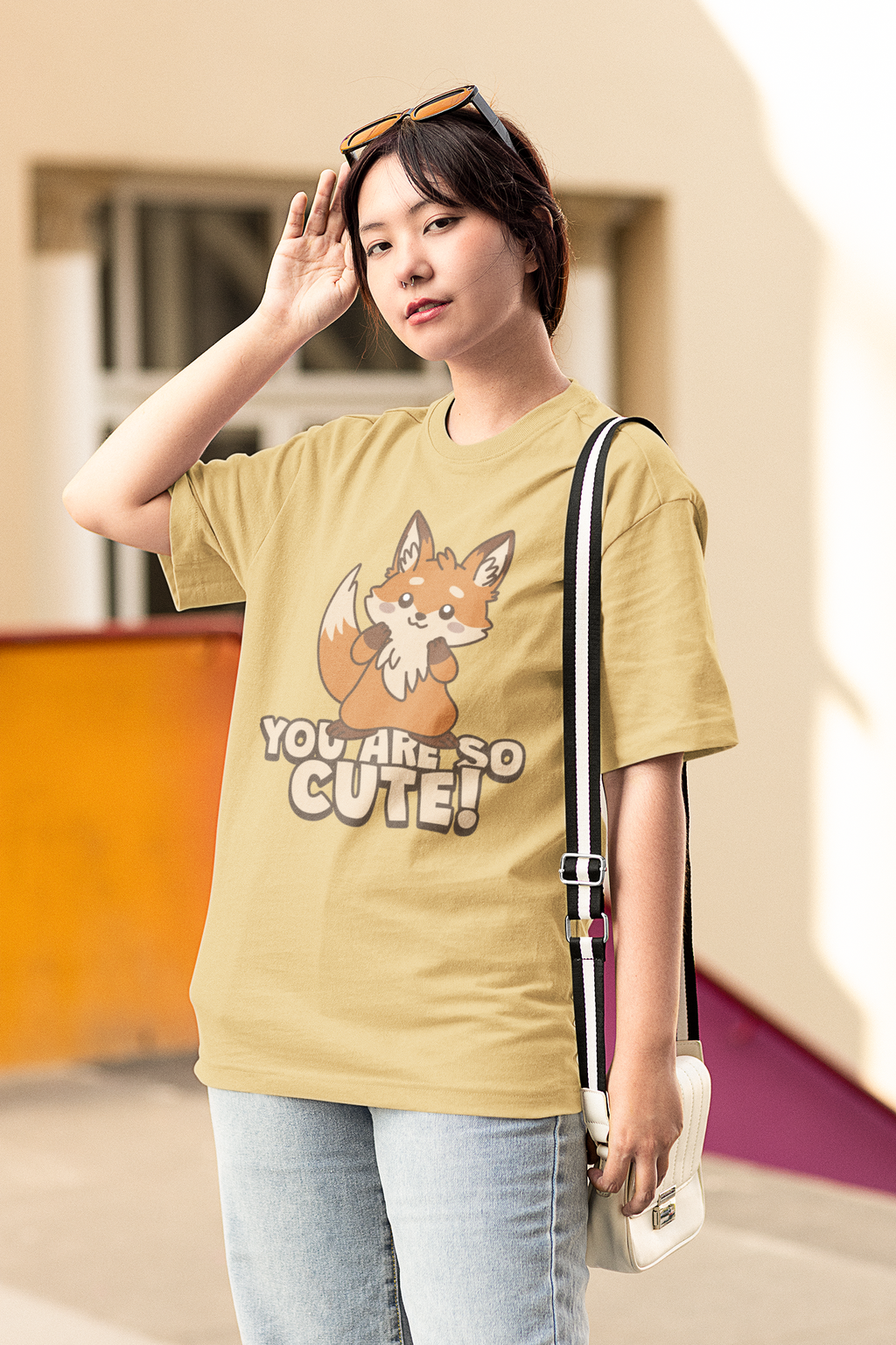 Woman wearing oversized beige T-shirt with cute fox graphic and text “You Are So Cute!” outdoors.